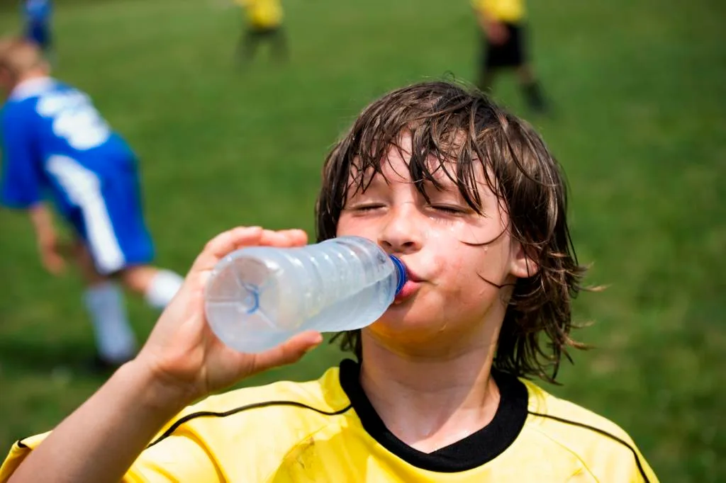 Thirsty soccer player drinking water on the sidelines of playing field.